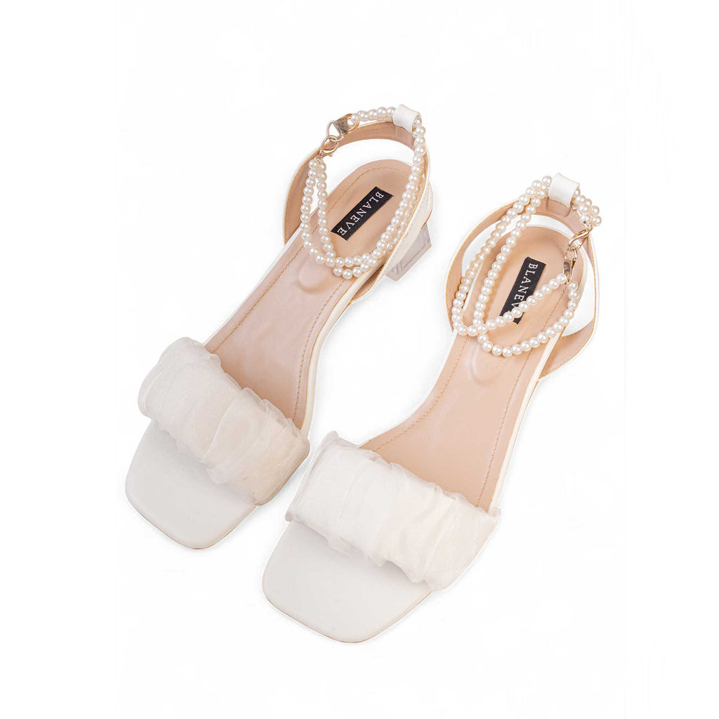 Angled view of BLANEVE Meringue white sandals showing square open toes, ruffled straps and pearl ankle detailing.