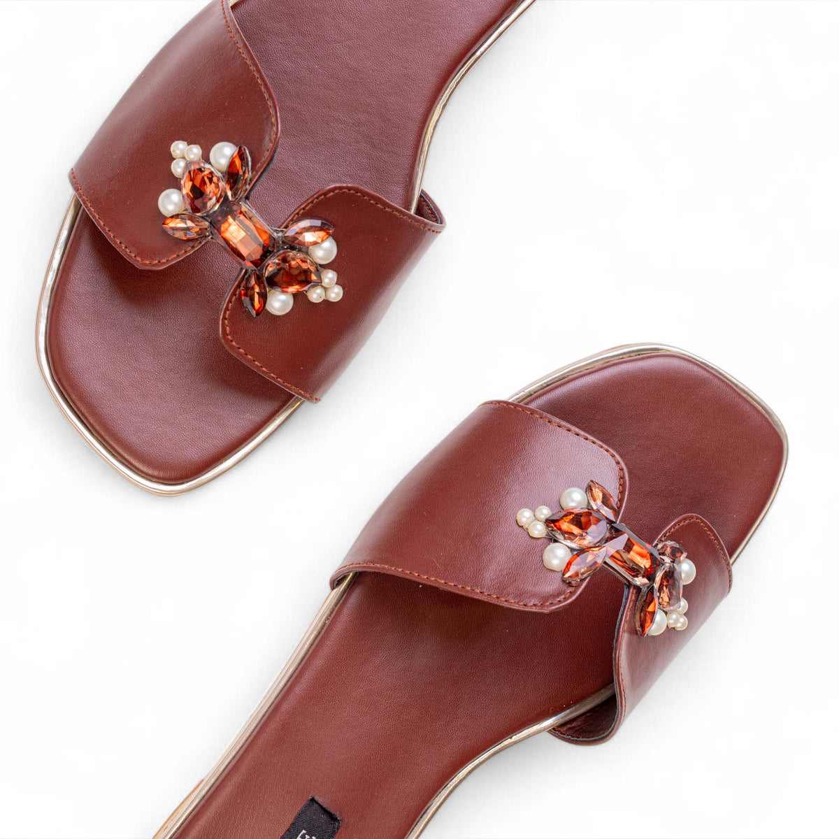 Close-up of pearls and faceted amber-toned stones forming bow details on BLANEVE Cove brown slides.