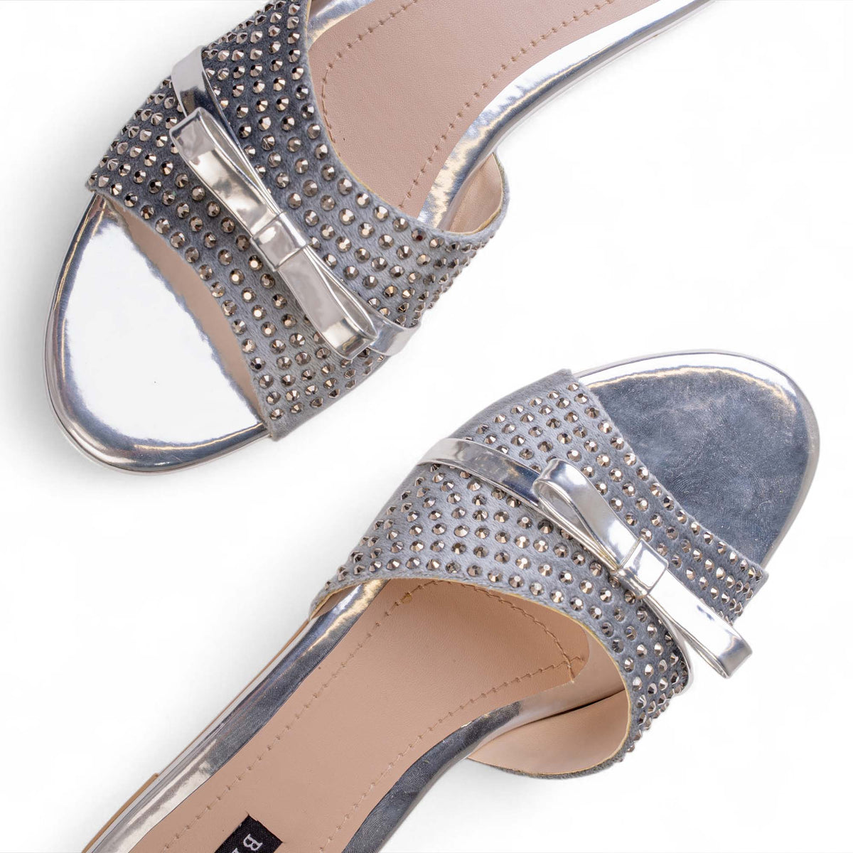 Close-up of crystal embellishments and metallic bow details on BLANEVE Starling silver-toned slides